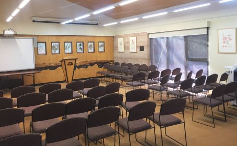 The conference room set up theatre-style with rows of cushioned chairs, a lectern, and a white board